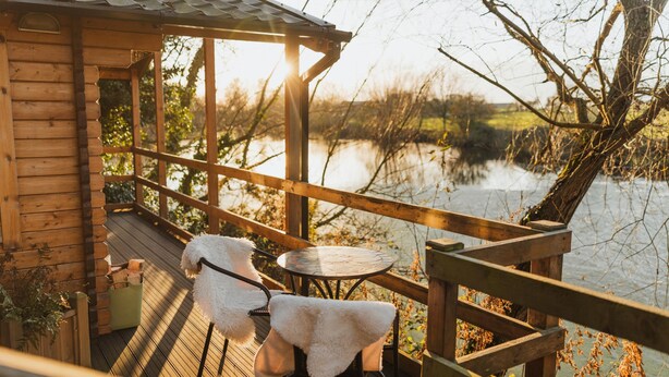Een houten terras met een tafel en stoelen, met uitzicht op een waterpartij.