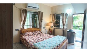 Une chambre à coucher avec un lit, des rideaux, un climatiseur, une lampe et une vue sur la verdure à l’extérieur.