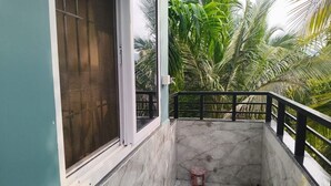 Un balcon doté d’un sol en marbre, d’une rambarde en métal et offrant une vue sur des palmiers.
