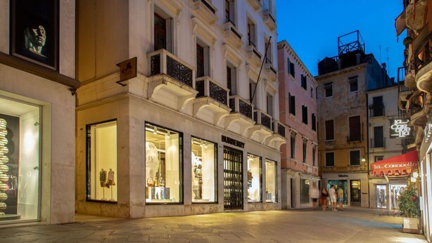 Vista di una strada che mostra un edificio storico con diversi negozi, tra cui il ristorante 'La Caravella'.