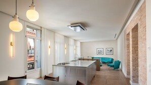 Una cucina moderna con isola centrale, zona pranzo con tavolo rotondo e angolo relax con sedie color acquamarina.