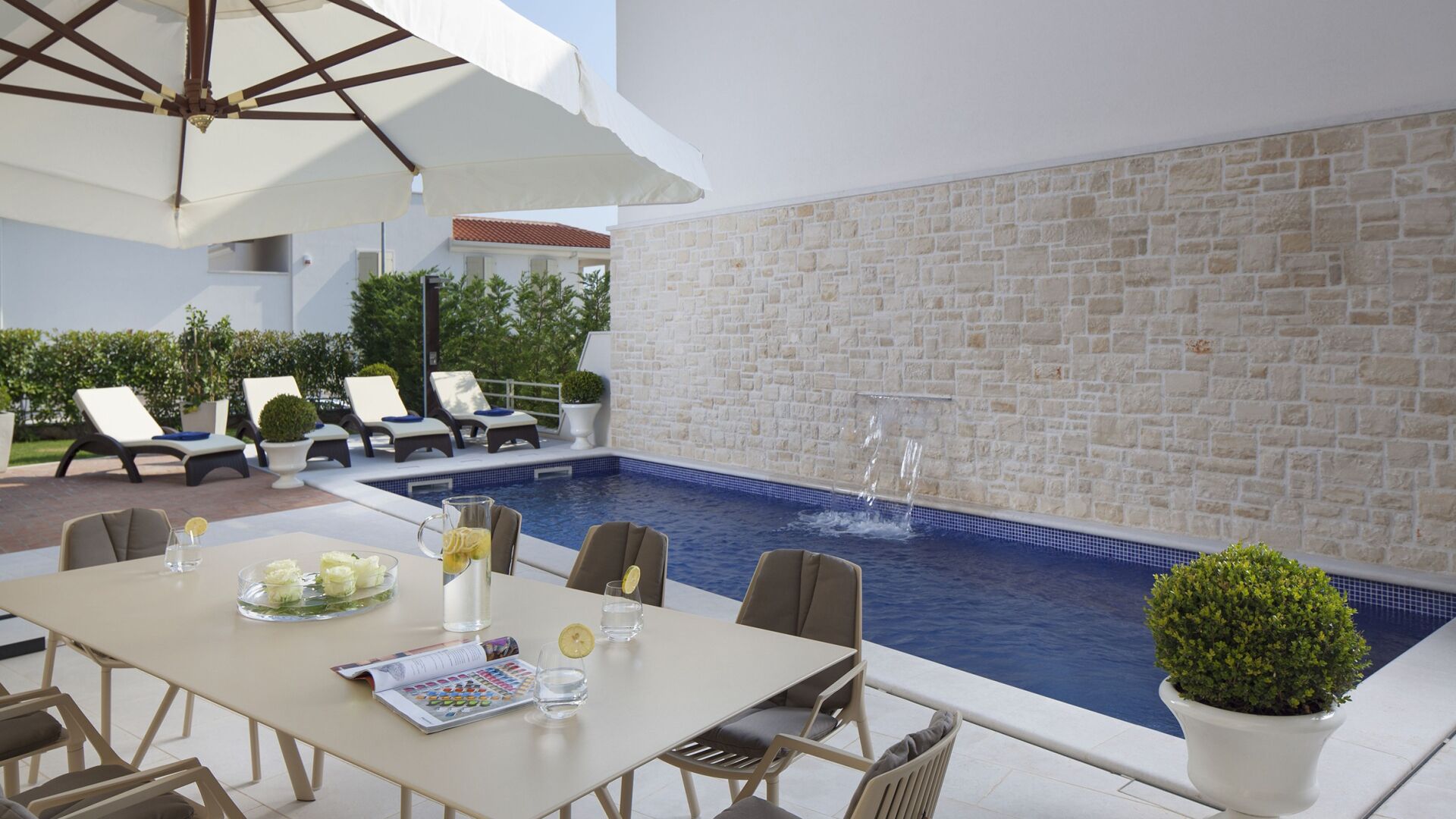 A poolside area with a table set for dining, lounge chairs, and a stone wall.