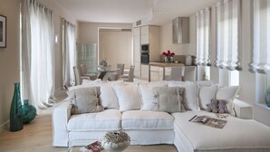 Una sala de estar moderna con un sofá seccional blanco, una mesa de centro de vidrio y un comedor con una mesa y sillas de vidrio.