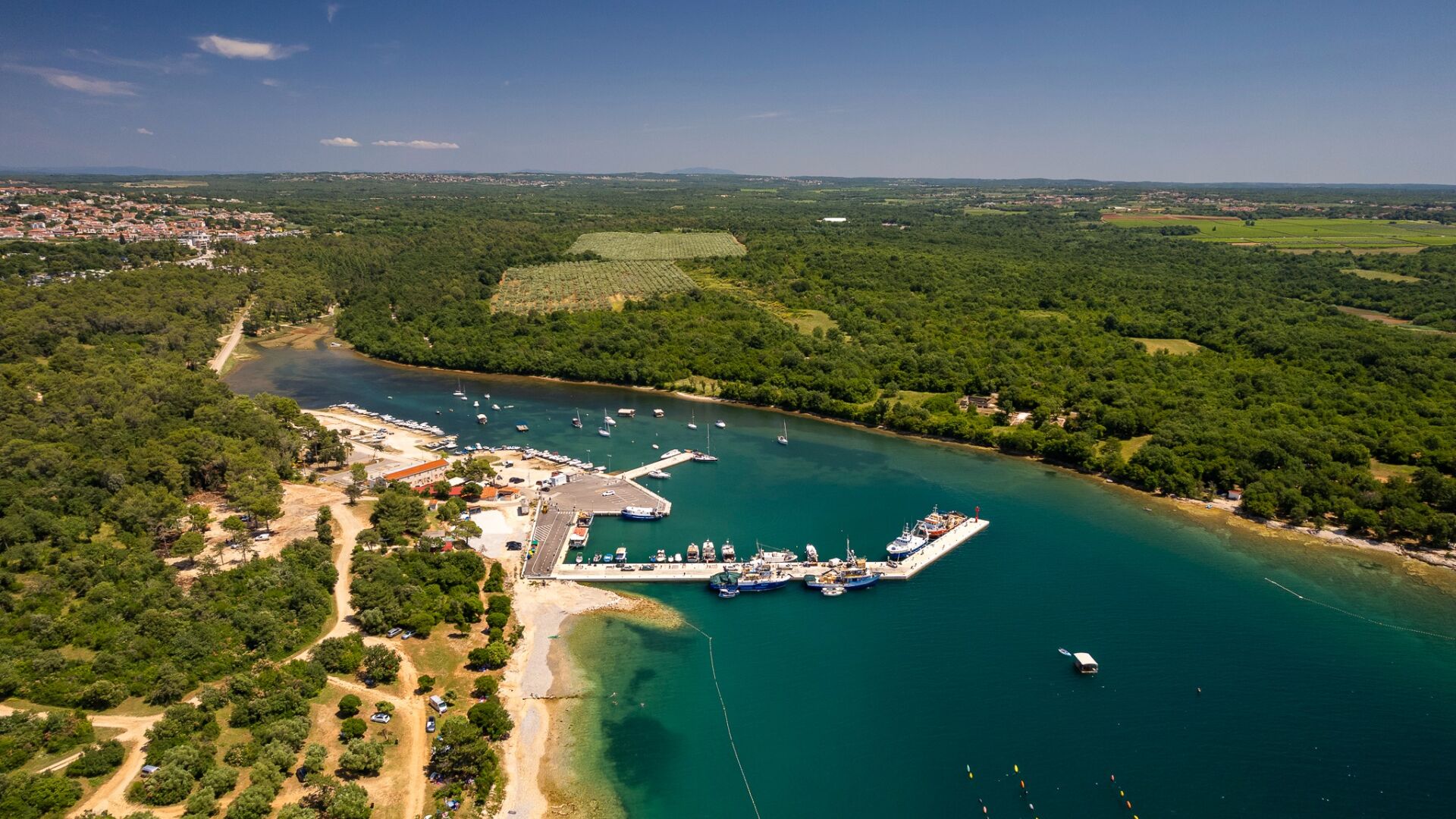 An aerial view of a coastal area with a marina, boats, and surrounding greenery.