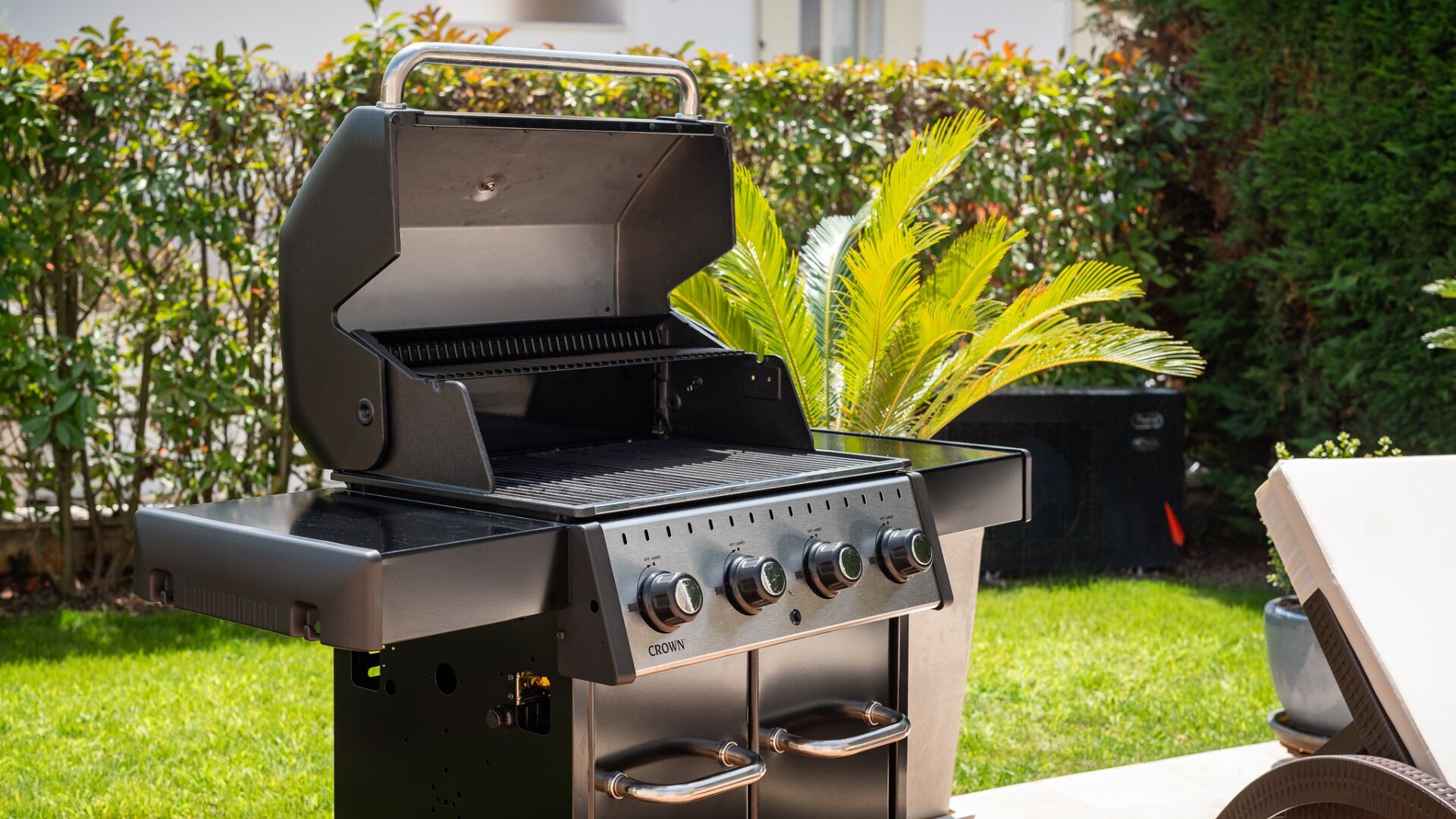 Un barbecue à gaz doté de quatre brûleurs et d’une étagère latérale, installé à l’extérieur, avec une haie et de l’herbe en arrière-plan.