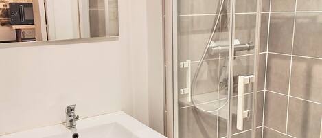 Un baño con ducha de vidrio, lavamanos blanco y espejo sobre él.