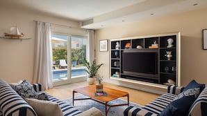 A living room with a pool view, a TV, and a bookshelf. - Villa Ginevra by Villas Guide (Tar)