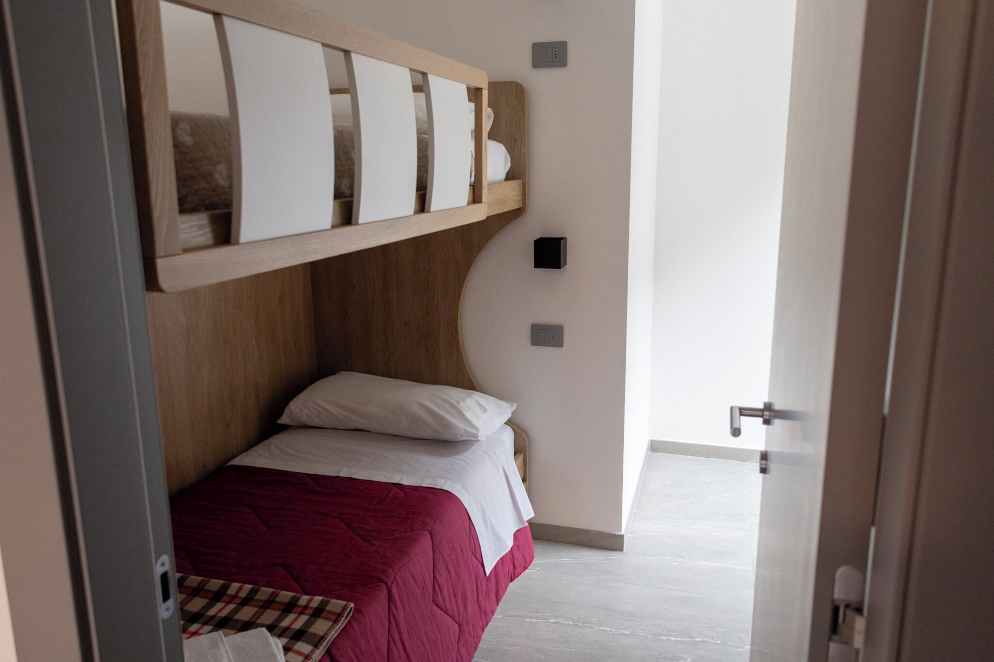 Une chambre avec un lit superposé, une table de chevet et une porte donnant sur une autre pièce.