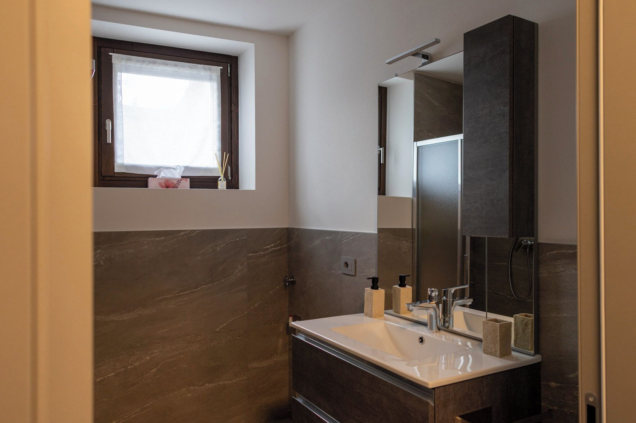 Een moderne badkamer met een grote spiegel, een raam en een wastafel.