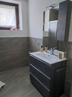 Une salle de bain moderne avec un grand miroir, des murs en marbre foncé et un lavabo blanc.