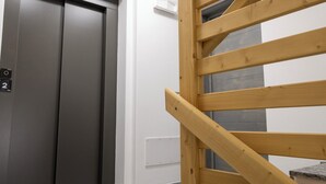 Μια ξύλινη σκάλα που οδηγεί σε ένα δωμάτιο με μια γκρι πόρτα και έναν λευκό τοίχο.