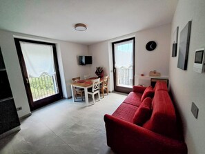 Un espace de vie compact comprenant un coin repas, un canapé rouge, un téléviseur fixé au mur et un balcon avec vue.