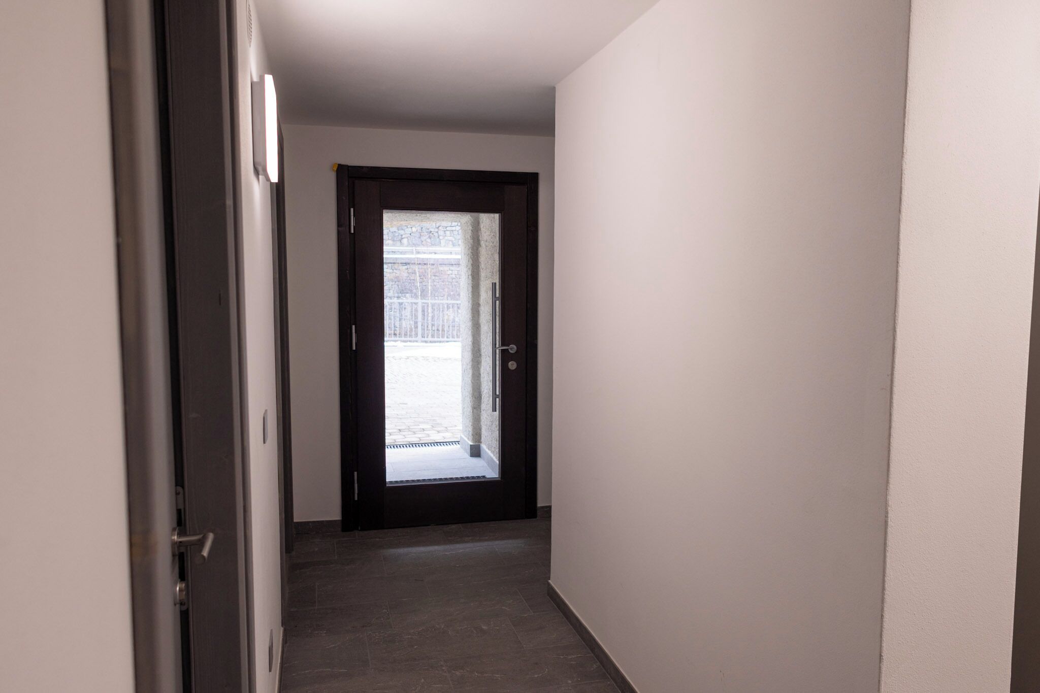 A narrow hallway with a dark door leading to a balcony.