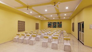 A conference room with rows of chairs covered in white and yellow sashes, ceiling fans, and artwork on the walls. - Hotel Hilltop by Fidato Hotels (Panhala)
