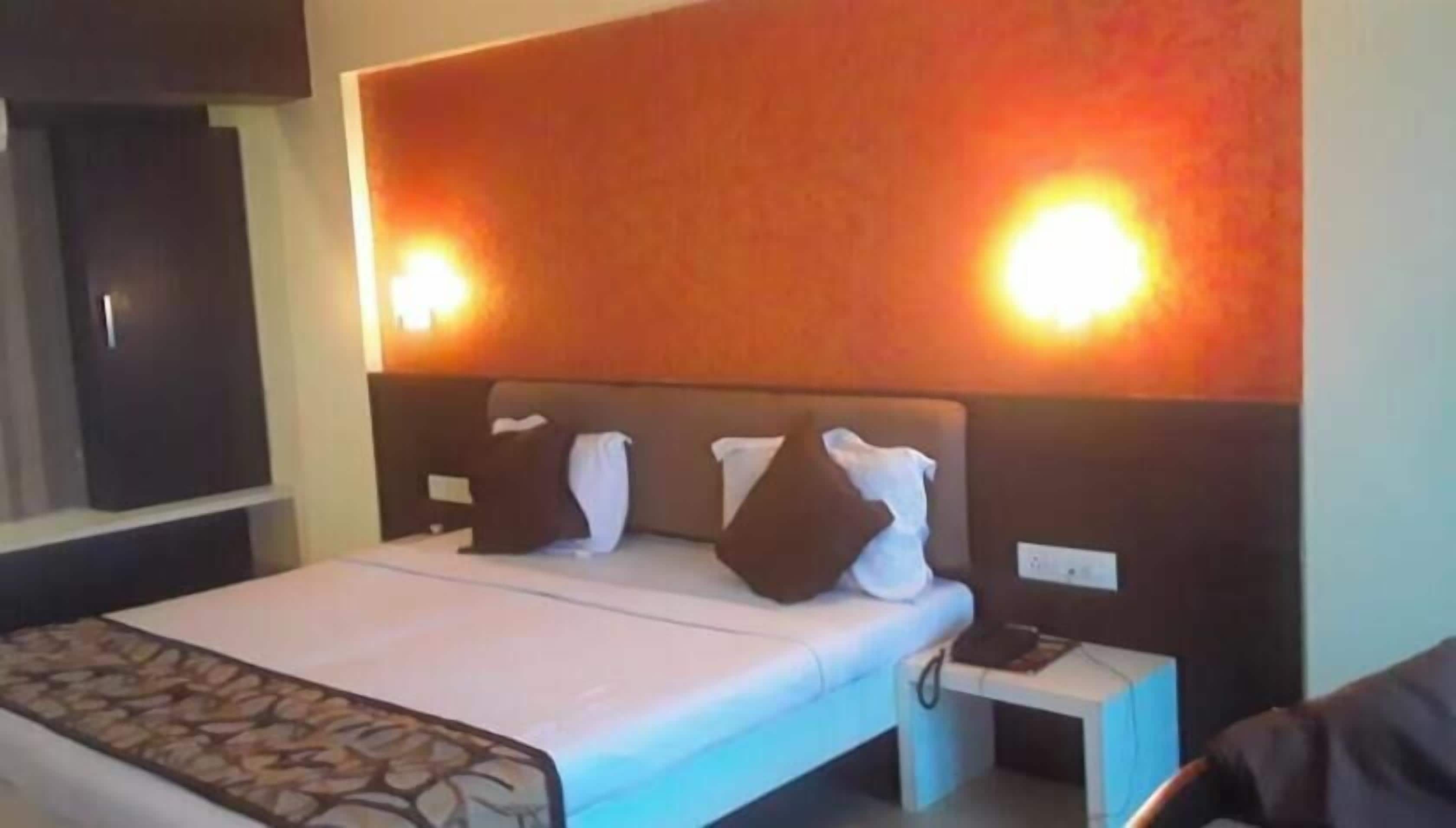 A hotel room with a bed, bedside tables, and a wall-mounted light fixture.