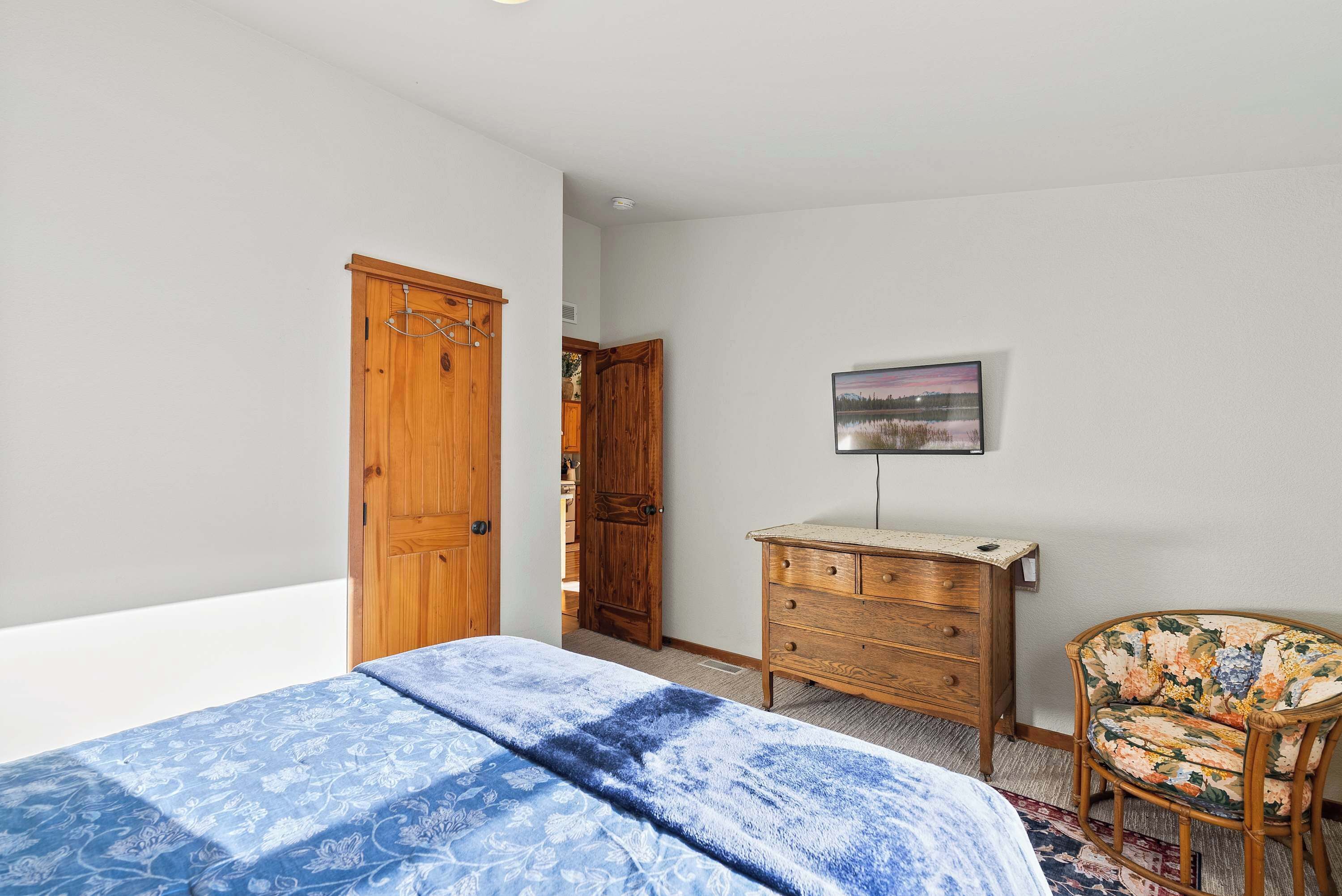 Une chambre à coucher avec un lit, une armoire en bois, une commode, une chaise et un tableau accroché au mur.