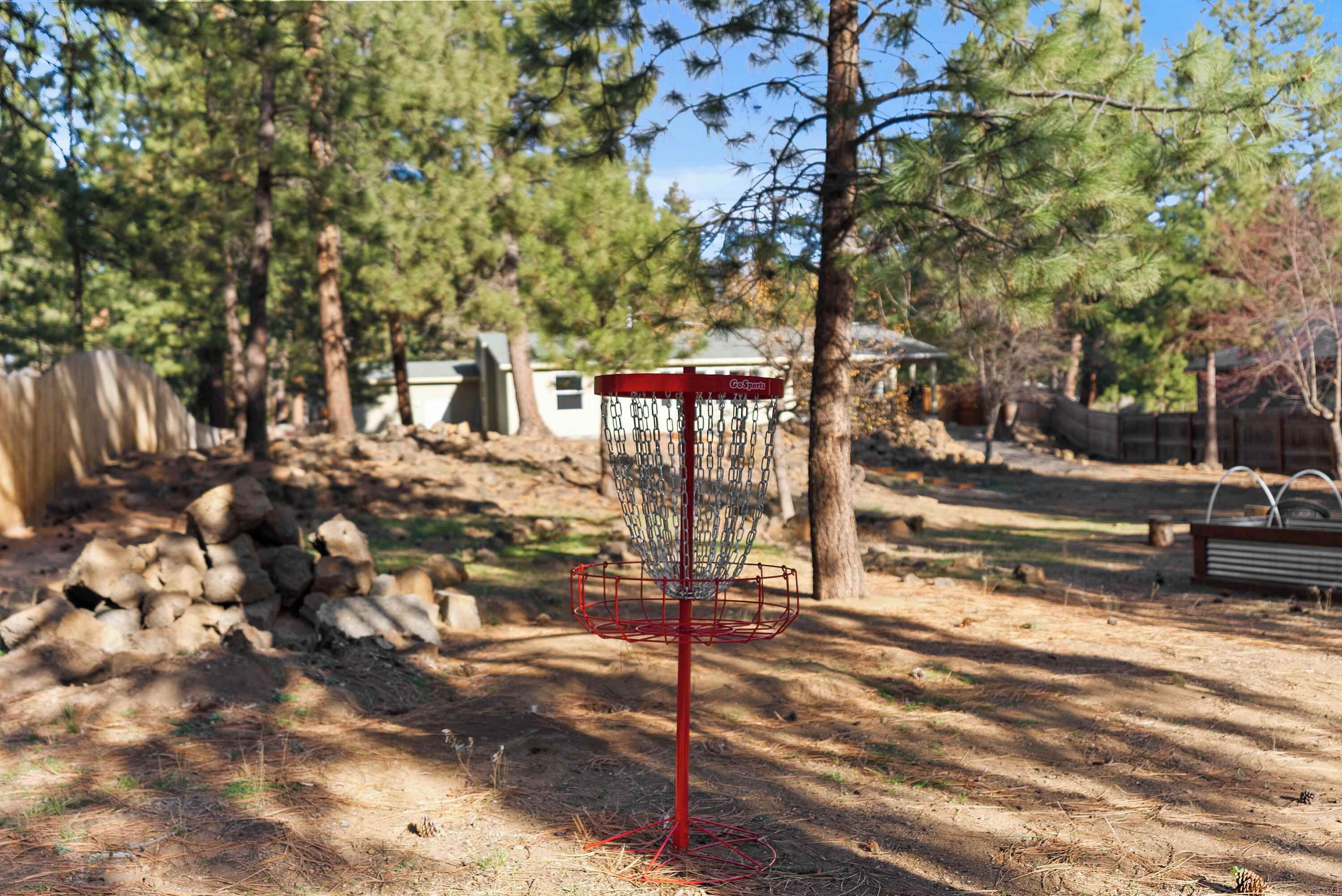 Un cistell de disc golf en una zona boscosa, amb arbres i un mont de pedres a prop.