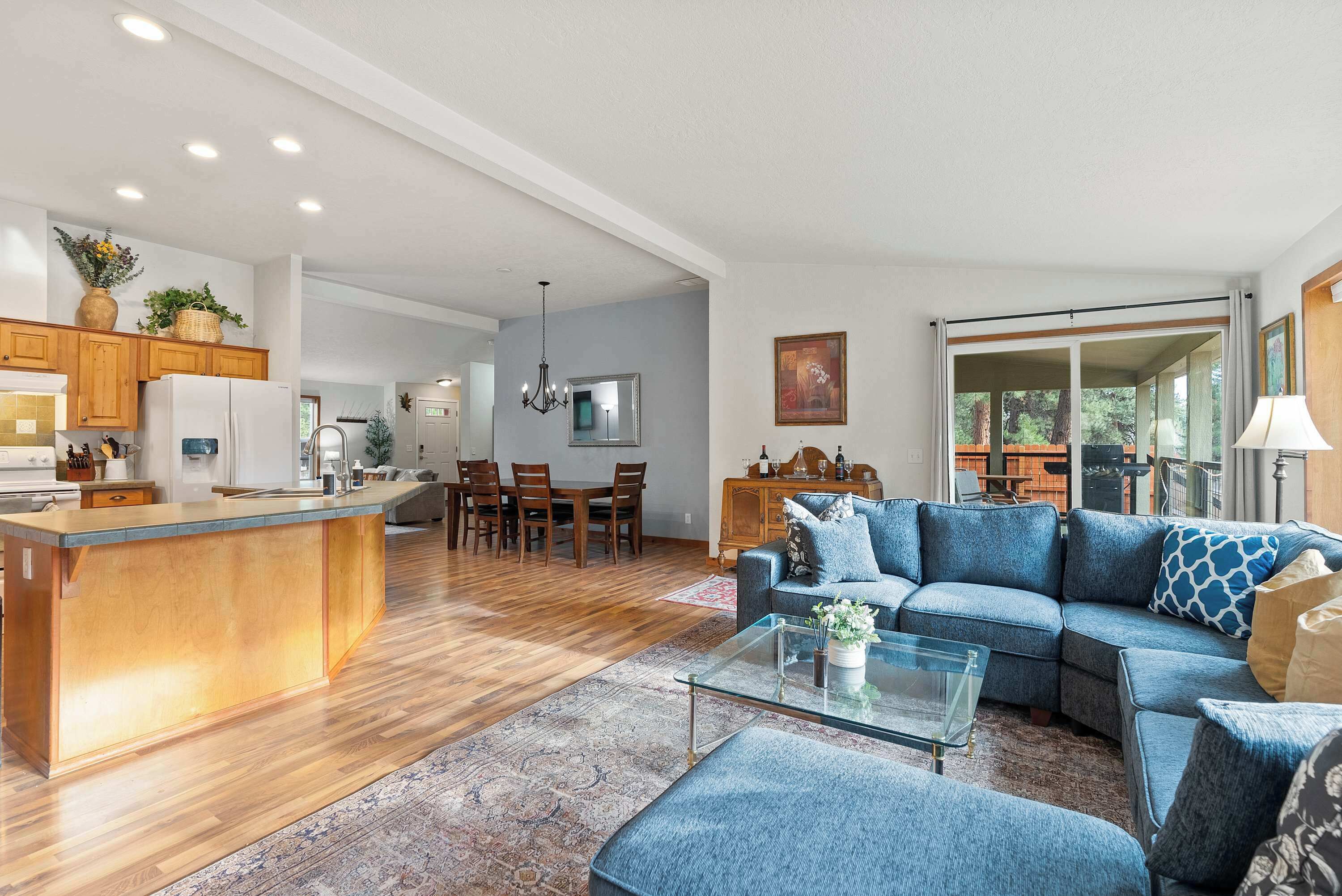 Un amplio salón con un sofá seccional azul grande, una mesa de centro de vidrio y una mesa de comedor de madera con sillas.