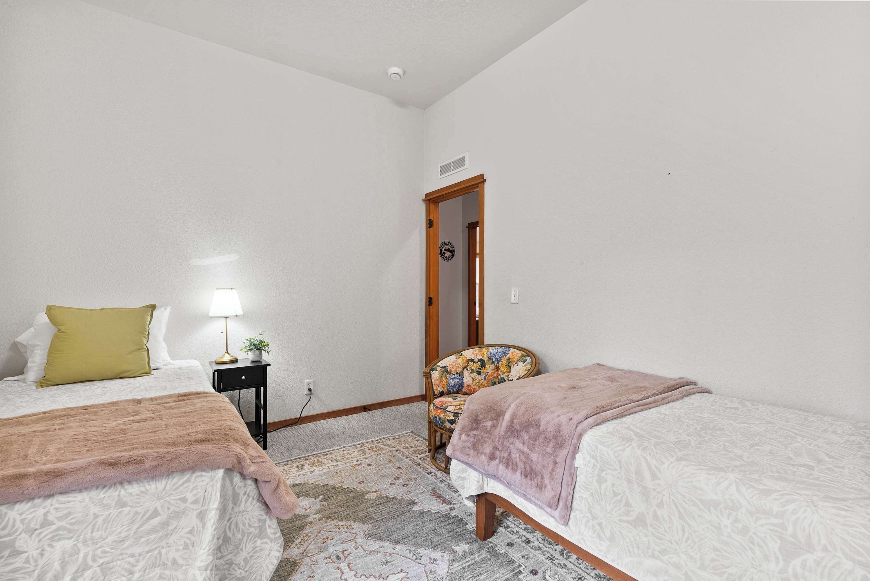 A bedroom with two beds, a nightstand, a chair, and a door.