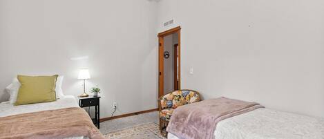 A bedroom with two beds, a nightstand, a chair, and a door.
