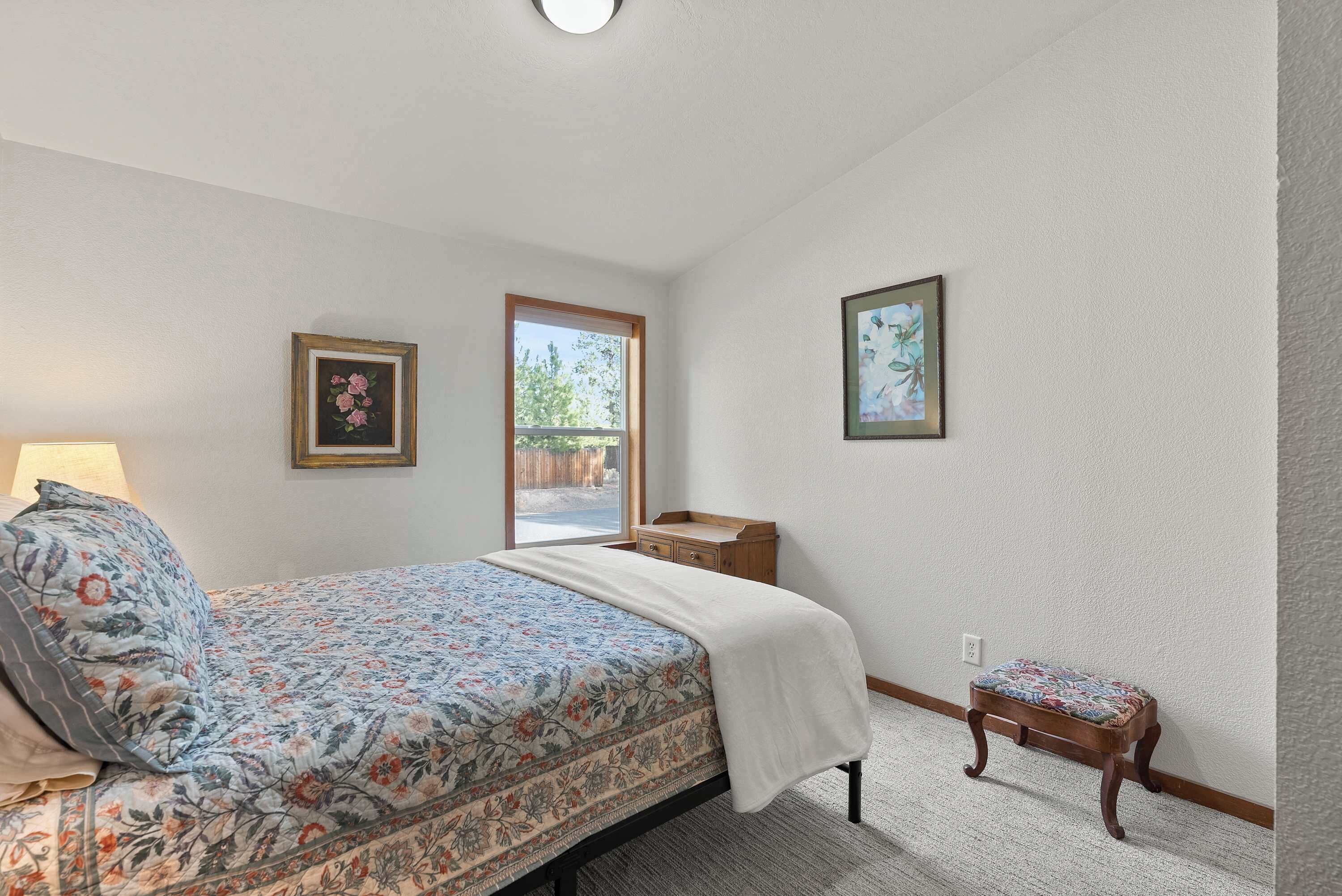 A bedroom with a bed, a bedside table, a small stool, and two framed pictures on the wall.