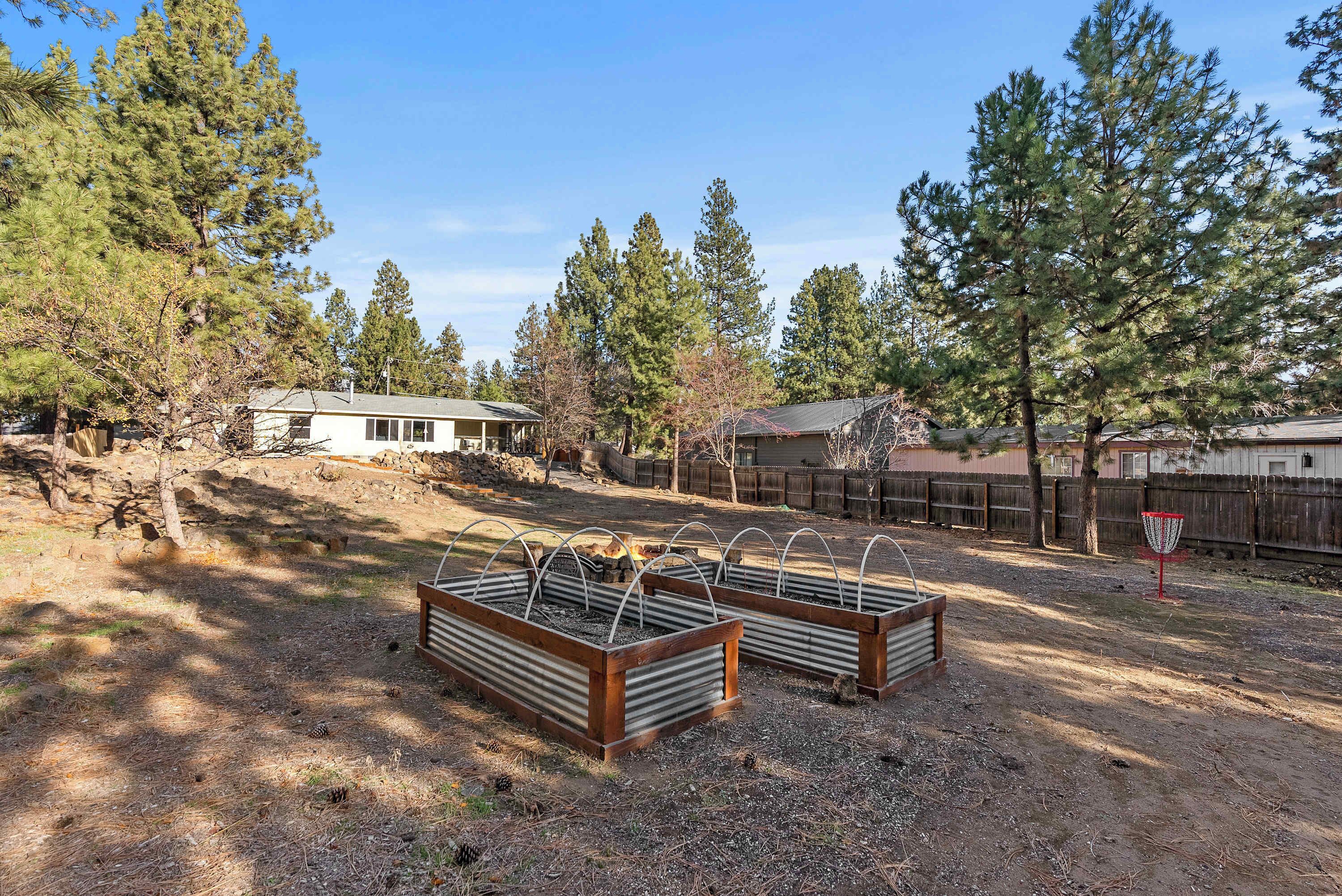 A fenced outdoor area with raised garden beds, a wooden fence, and a house in the background.