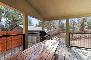A covered outdoor patio with wooden tables and a barbecue grill. - Just Around the Bend For 8 (Bend)