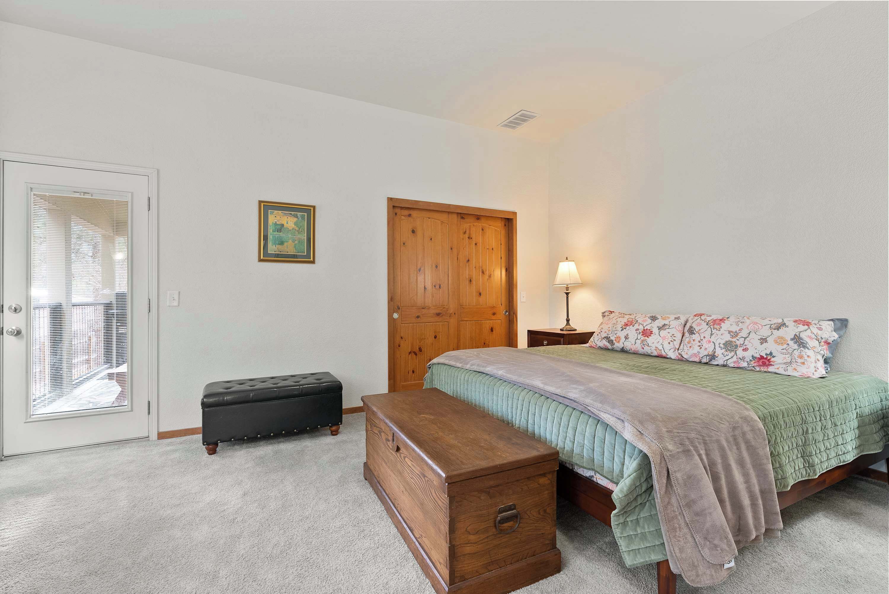 A bedroom with a bed, a wooden chest, a bench, a wardrobe, and a window with blinds.