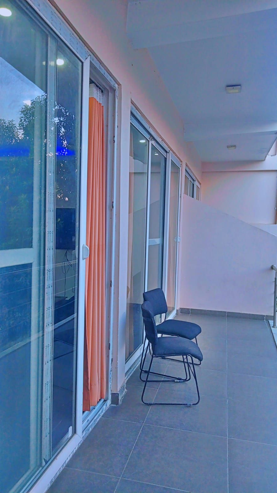 A balcony with a chair, large windows, and orange curtains.