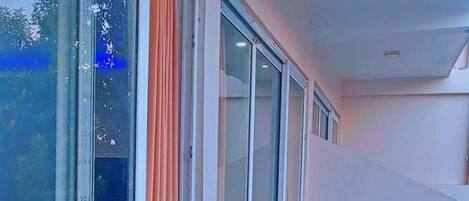 A balcony with a chair, large windows, and orange curtains.