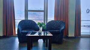 A room with two armchairs, a small table with a vase, and a large window with curtains. - Diamond Vaishali (Kullu)