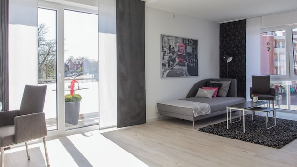 A modern living room with a sofa, armchairs, a coffee table, and a large window with a view of the street. - Refugium 2 (Emsdetten)