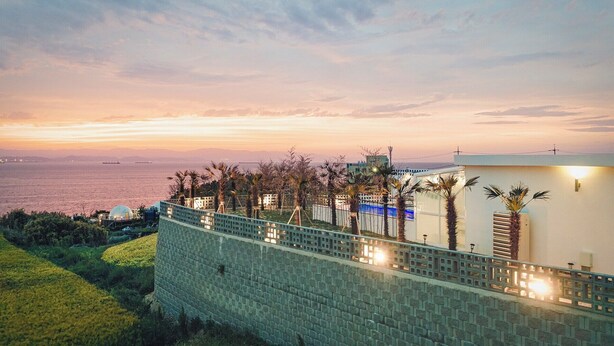 Ein Küstenhotel mit Mauerwerk, Palmen und Blick auf das Meer bei Sonnenuntergang.