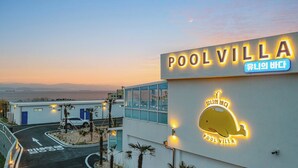 Ein Gebäude mit einem leuchtenden Neon-Schild mit der Aufschrift „POOLVILLA“ und einem Neon-Walsymbol.