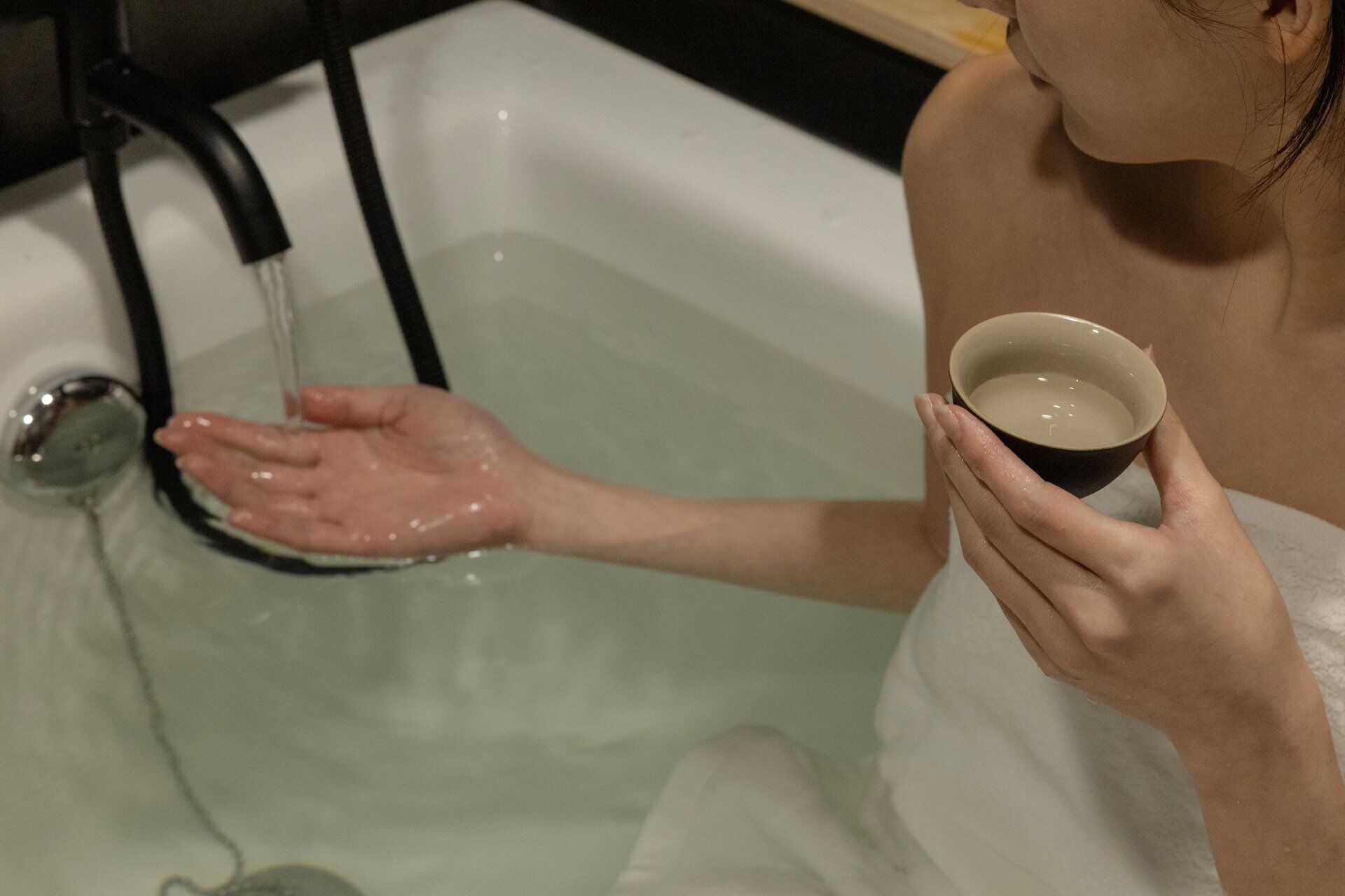 A person in a bathtub holding a cup of water.