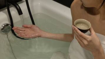 A person in a bathtub holding a cup of water.
