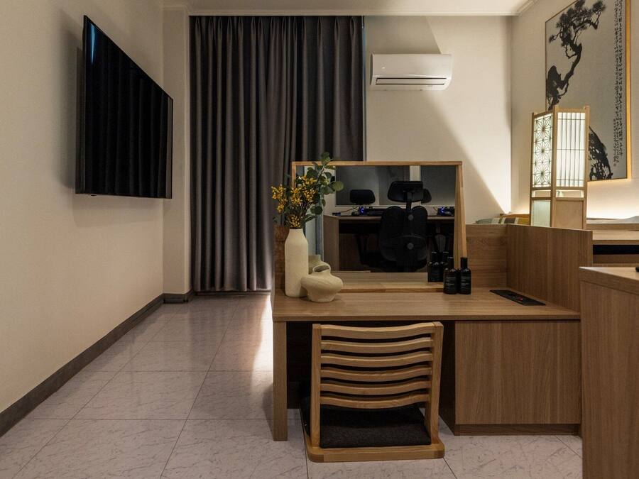 A hotel room with a desk, chair, TV, air conditioning unit, and a decorative mirror.