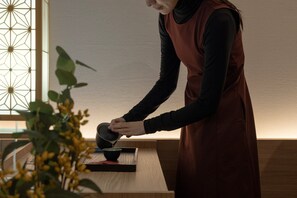 Una persona sirve té en una taza sobre una mesa de madera en una habitación con una ventana de diseño geométrico.