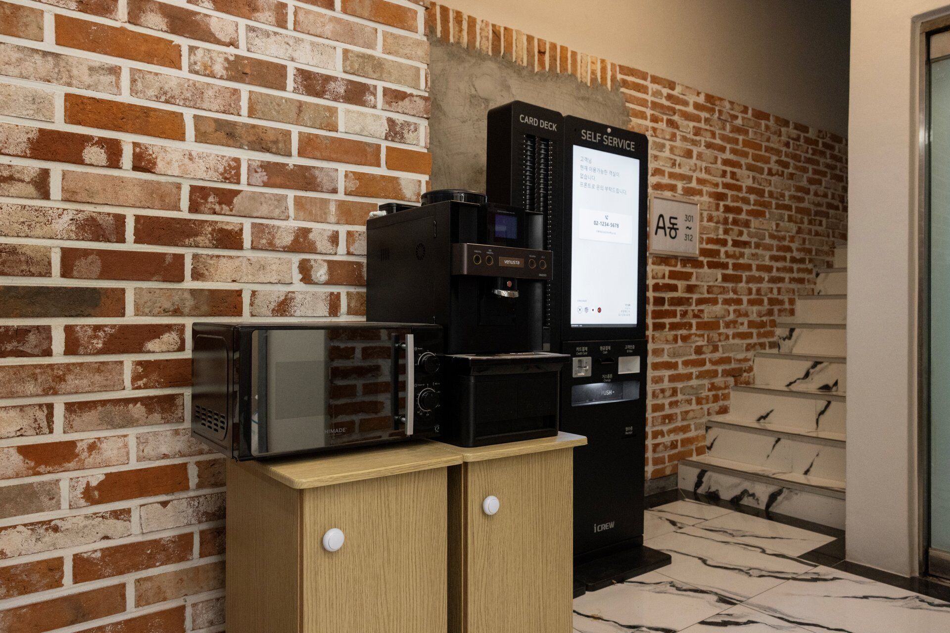 Una máquina de café automática y un microondas sobre un mueble de madera frente a una pared de ladrillo.