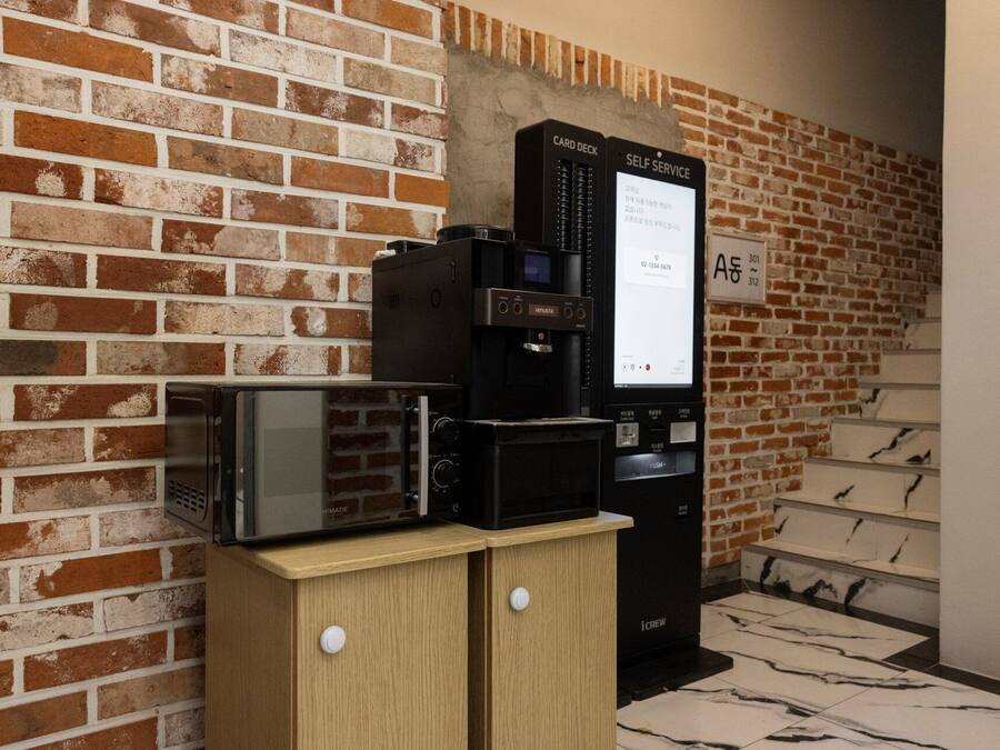Una máquina de café automática y un microondas sobre un mueble de madera frente a una pared de ladrillo.
