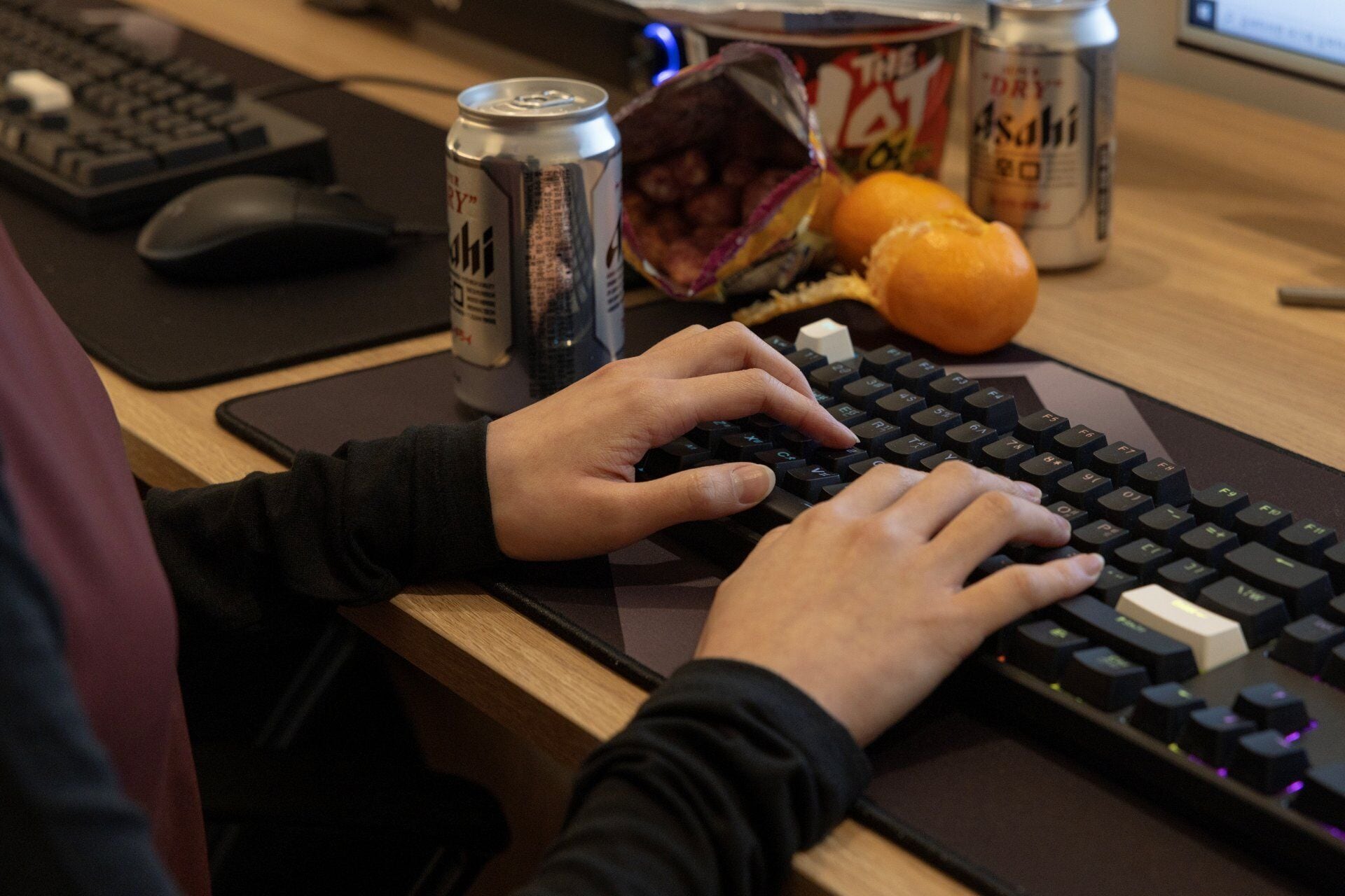 Una persona escribiendo en un teclado mecánico, con una lata de bebida energética y un refrigerio a su lado.