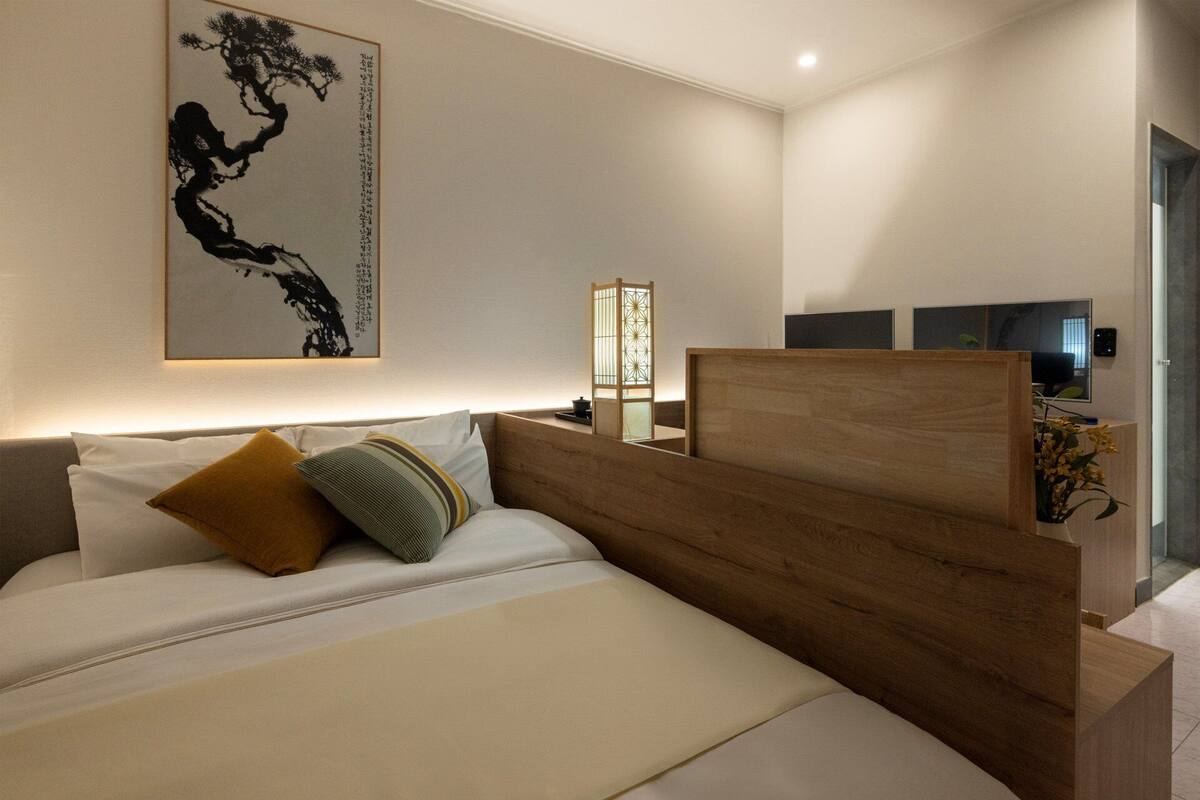 Una moderna camera d'albergo con una testiera in legno, un letto grande, un comodino, una TV e un elemento decorativo a parete.
