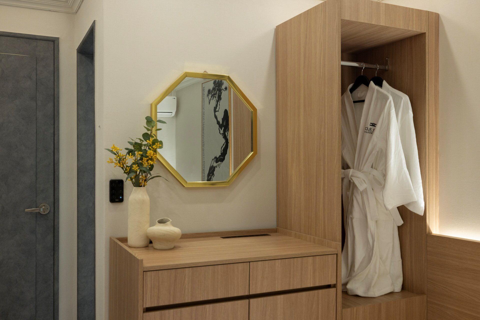 A modern bathroom with a wooden vanity, a mirror with a gold frame, and a robe hanging in a wooden closet.