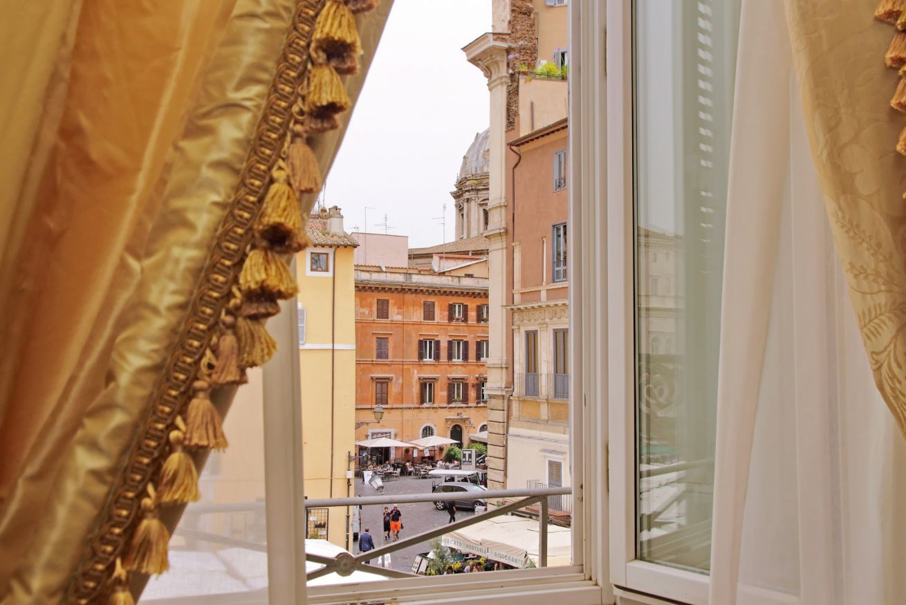 A view from a window with ornate curtains, overlooking a street with buildings and a café.