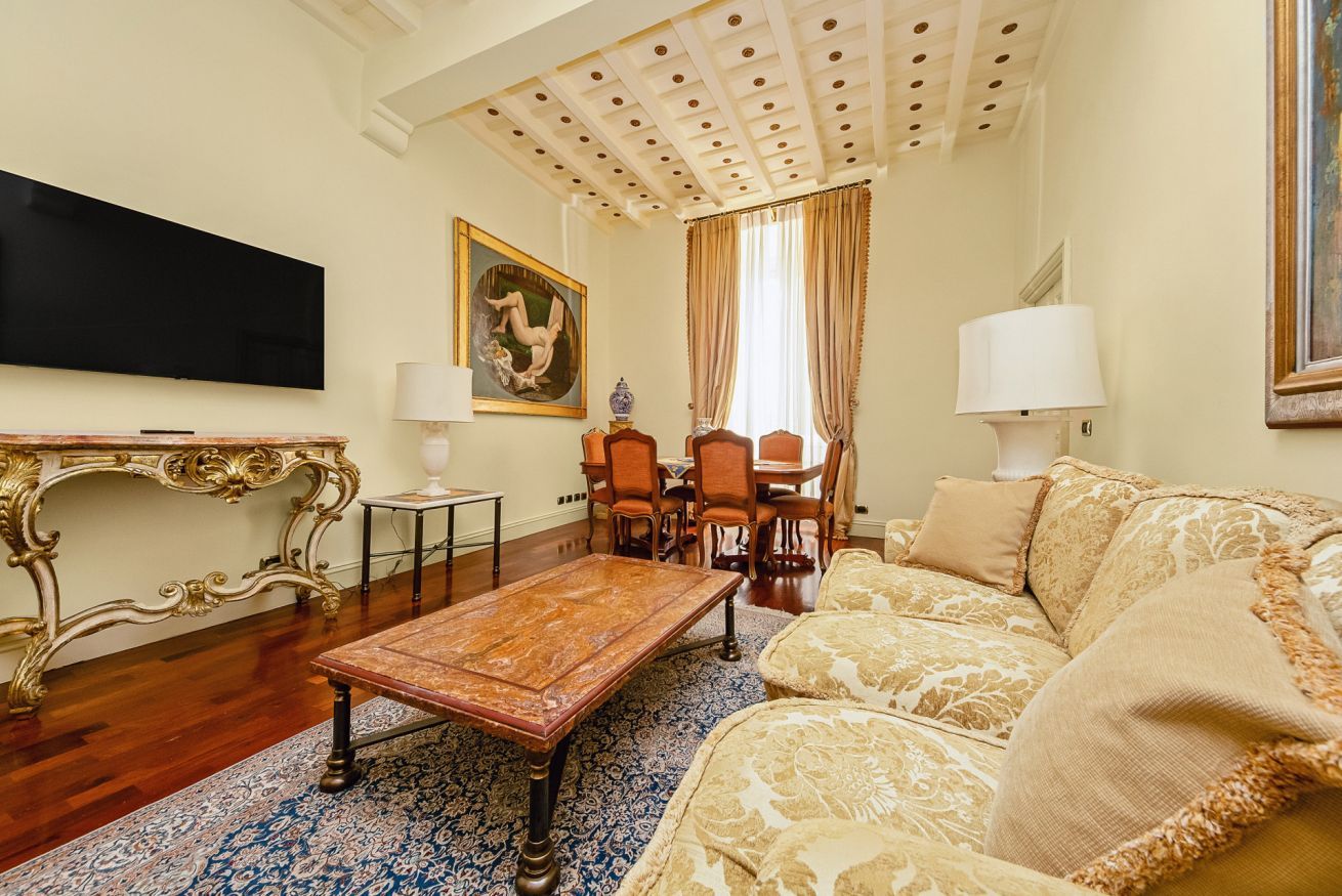 Un salon comprenant une table basse en bois, un canapé, un téléviseur fixé au mur et un coin repas avec des chaises et une table.