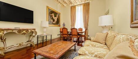 Un salon comprenant une table basse en bois, un canapé, un téléviseur fixé au mur et un coin repas avec des chaises et une table.