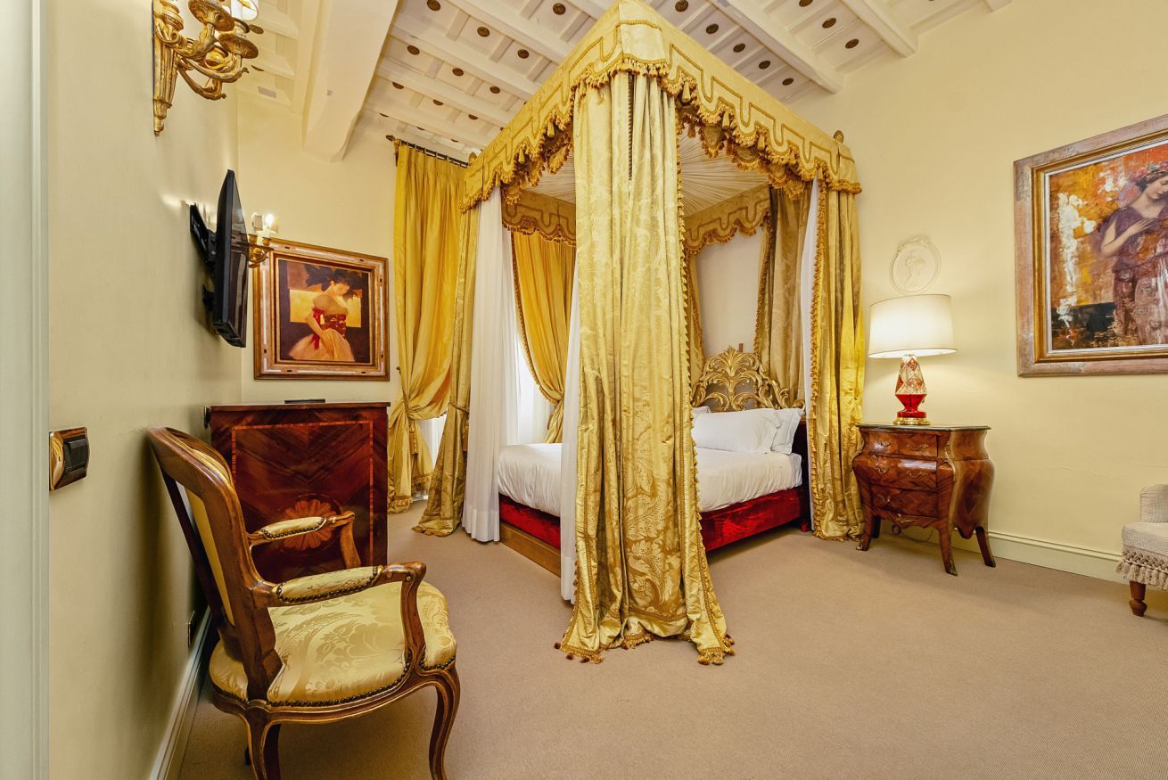 A luxurious bedroom with a four-poster bed, a wooden chair, a bedside table, and a painting on the wall.