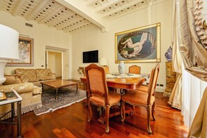 A spacious living room with a wooden dining table, comfortable seating, and a large painting on the wall. - Magnifica Residenza a Campo de' Fiori (ROMA)