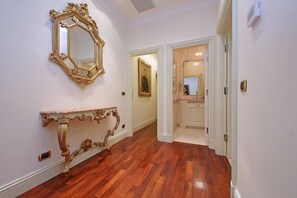 Ein Flur mit Holzboden, einem spiegelnden Goldrahmen und einem weißen Konsolentisch.