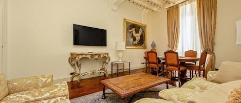 Una sala de estar con televisor de pantalla plana, un cuadro, una mesa de comedor con sillas y sofás estampados.